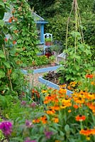 Summer garden of mixed vegetable and flower beds, foreground with Monarda 'On Parade' and Helenium 'Sahin's Early Flowerer' .

