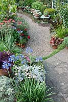 Paved and gravel path through colourful arrangements of terracotta pots. Planting of Agapanthus, Tradescantia, Argyranthemum Senecio cineraria,  Ficus carica 'Brown Turkey, Eucomis 'Sparkling Burgundy',   at Southlands, July 