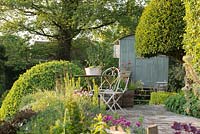 Patio area with metal bistro set, Shepherd's Hut in background and clipped Prunus lusitanica and Buxus sempervirens, Alnus glutinosa - Alder in background