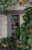 Exotic timber statue in wall alcove surrounded by philodendron and Pyrostegia venusta, Flame vine. 