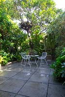 Inner city Sydney courtyard with a white metal table setting with a retro concrete log pot planted with succulents amongst a garden featuring assorted bromeliads, rhipsalis and various sub-tropical plants.