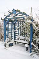 Snow covered garden arbor with garden seat and potted plants, Norfolk, UK, December