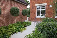 View towards house with sandstone path leading past Buxus lollipops and herbaceous borders