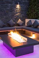 Secluded seating area with a dry stone slate wall and propane fire pit emitting purple light