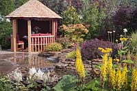 A natural stone edged pond and wooden gazebo. Garden: 'Reflections' at RHS Tatton Park Flower Show 2012