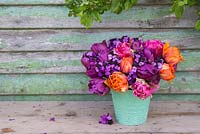 Teal vase containing Erysimum 'Bowles Mauve', Tulipa 'Orange Princess', 'Purple Peony' and 'Chato'