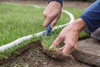 Using a stanley knife to cut newly laid turf to shape, following along the rope guide