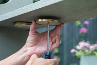 Screwing glass jar lids underneath the book shelf