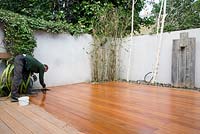 Applying wood oil to finished decking in small urban garden