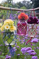 A floral display of glass vases in woven nets, hanging above a cluster of Verbena bonariensis