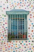 Pale blue painted window surrounded by artificial flowers with grille and pots of pelargoniums, Cordoba, Spain