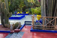 Cacti beside a blue painted fountain and pool in the Jardin Majorelle. Created by Jacques Majorelle and further developed by Yves Saint Laurent and Pierre Bergé, Marrakech, Morocco