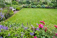 Summer borders surrounding lawn area with wooden bench. Clematis'Emilia Plater', Rosa 'Cornelia' and Rosa 'Red Leonardo da Vinci'. Sarina meijer garden