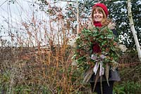 Sheree King holding a traditional christmas wreath made with Eucalyptus gunnii, Rosa 'Bonica' rose hips, Variegated Ivy, Ilex aquifolium, Cotoneaster lacteus, Pinus nobilis, Godetia and Miscanthus sinensis seed heads