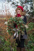 Sheree King holding a traditional christmas wreath made with Eucalyptus gunnii, Rosa 'Bonica' rose hips, Variegated Ivy, Ilex aquifolium, Cotoneaster lacteus, Pinus nobilis, Godetia and Miscanthus sinensis seed heads