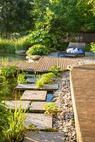 Transition zone from the pond to wooden deck with gravel, flagstones and plants including Caltha palustris, Darmera peltata, Hedera arborescens and Quercus pontica