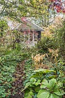 Summerhouse in the wild garden framed by berries of Euonymus hamiltonianus, liquidambar and dogwood.