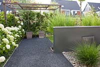 Pergola with vine and split paving. Low maintenance planting by Hydrangea 'Annabelle',  Calamagrostis x acutiflora and Pennisetum