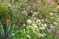 Rusty metal Allium shaped sculptures in mixed border.  Pennisetum Villosum, Verbena Bonariensis and Stipa Gigantea.  Late summer in owner of Daisy Roots Nursery's own private garden.  Anne Godfrey's garden in Hertfordshire. 