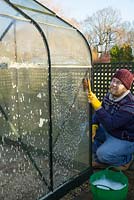 Man cleaning dirty glass panes of a small patio greenhouse