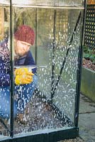 Man cleaning dirty glass panes of a small patio greenhouse