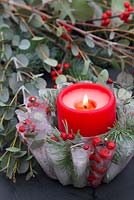 A frozen Jelly mould candle bowl with a lit candle. Constructed from Pine foliage, Eucalyptus and Ilex verticillata berries