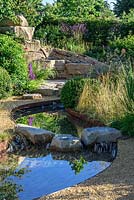 Rock stepping stones over a water rill, Cercidiphyllum japonicum with Prunus lusitanica and Panicum virgatum 'Northwind' - Zoflora: Outstanding Natural Beauty, RHS Hampton Court Palace Flower Show 2016