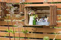 Decorative flower displays in crates used as shelves on the wooden panel fencing. Katie's Lymphoedema Fund: Katie's Garden, RHS Hampton Court Palace Flower Show 2016. Design: Noemi Mercurelli and Carolyn Dunster