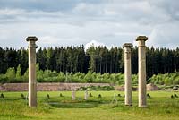 Ionic Columns in the classical Greek tradition stand in the Landscape Park with the neighbouring forest behind.