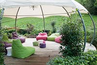Modern garden with decking and multi coloured soft cushion seats under gazebo. 