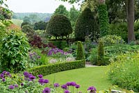 A cottage garden with circular lawn and raised wildflower mound. The formal structure is created by low box hedging, conical shaped yews and domed holly trees.