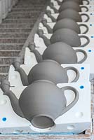 A line of teapots, newly solidified, with one half of the mould removed so they can dry out.