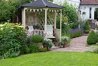 Overlooking the lawn and borders, a gazebo flanked by pots of lavender and marguerites. Beyond, a pebble, lavender lined path leads to the patio.