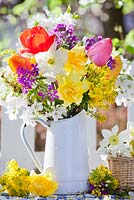 Display of spring flowers in jug. Daffodils, tulips, mahonia, lunaria and cherry blossom branches.