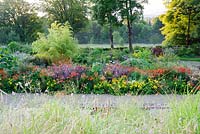 Hot beds viewed from above full of vivid red, orange and yellow herbaceous perennials and shrubs including yellow Leontodon rigens, orange Lilium lancifolium, Cotinus 'Grace', Dahlia australis and Crocosmia 'Lucifer'.