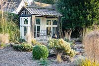 Summerhouse at the top of the gravel garden is framed by grasses, evergreen shrubs including box and pine and herbaceous perennials. Windy Ridge, Little Wenlock, Shropshire, UK