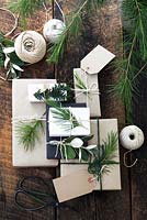 Lots of presents wrapped with brown and white paper and fastened with string, with gift tags and string.  Decorated with fir tree, yew tree and silvery foliage, with scissors