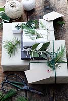 Lots of presents wrapped with brown and white paper and fastened with string, with gift tags and string.  Decorated with fir tree, yew tree and silvery foliage, with scissors