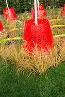 Anemanthele lessoniana and Echinops ritro surround red pendulum containers - Kinetica, RHS Hampton Court Palace Flower Show 2017