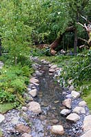 The Zoflora and Caudwell Children's Wild Garden. Shallow stream in woodland garden with edging of rocks and pebbles. Designers: Adam White and Andree Davies. Sponsors: Zoflora. RHS Hampton Court Palace Flower Show 2017