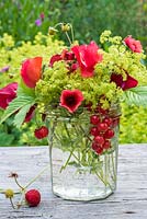 Summer floral arrangement in glass jar with red sweetpeas, potentialla, fragaria vesca, red currants and alchemilla mollis