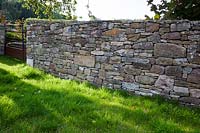 Detail of a drystone boundary wall and rusty iron gate in a country garden