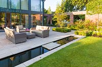 A patio area, with seating and a rill, in a modern Cheshire country garden, designed by Louise Harrison-Holland. Planting includes box hedging, Amelanchier lamarckii and Stipa tenuissima