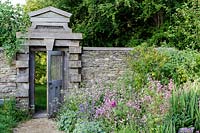 Hanham Court Gardens, Bristol. Early summer garden with mixed informal planting and rustic wooden gate in garden wall