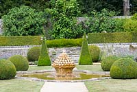The lawn terrace with ornate fountain and pool Buxus balls and pyramids and stone wall with terrace beyond at Brecy Gardens, Normandy, France