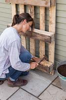 Woman attaching wood to bottom of pallet to ensure that there is a surface for the plants to sit on