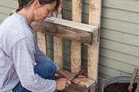 Woman attaching wood to bottom of pallet to ensure that there is a surface for the plants to sit on