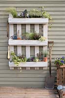 White pallet planter with garden tools and a mix of flowers, grasses and herbs