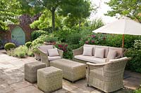 Wicker furniture on patio in summer with Rosa, clipped topiary and mixed decorative containers