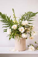 Flower arrangement with white roses, foxgloves, jasmine and ferns in cream jar